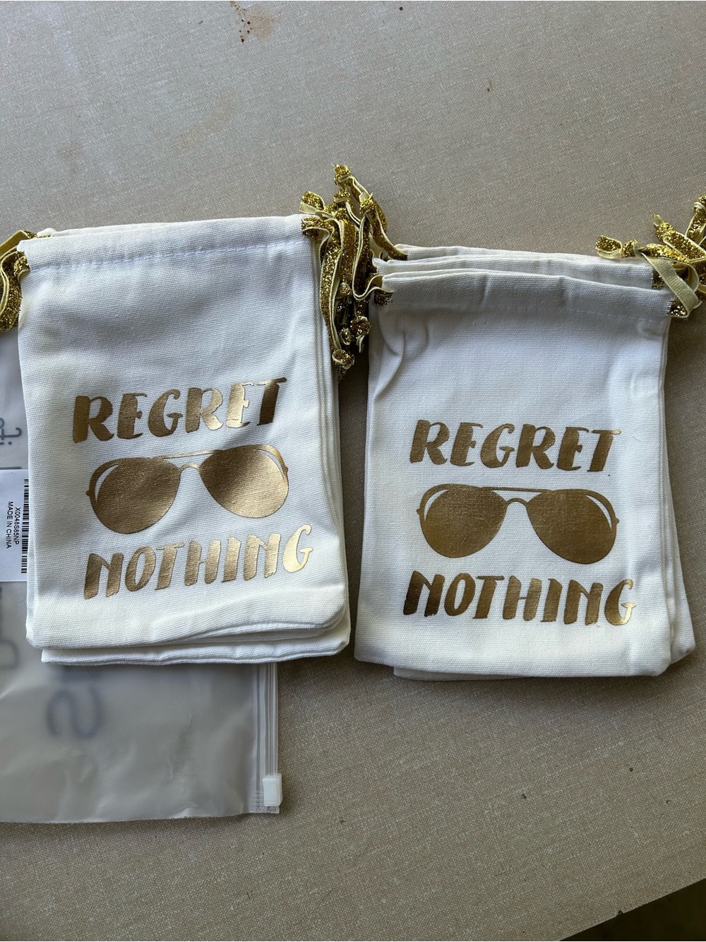 White Drawstring Pouches with Gold 'Regret Nothing' Print